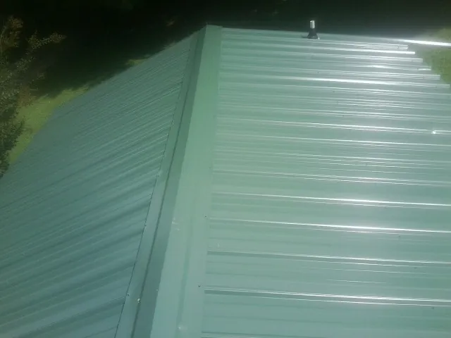 New green metal panels meeting at the ridge of a roof — Flat Roof Repair work by our crew in Andrews