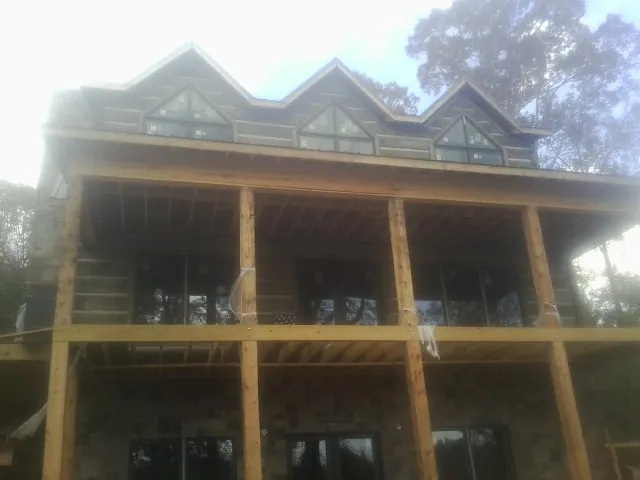 Dormers and porch framing on a large log home under construction — Roof Coating work by our crew in Andrews